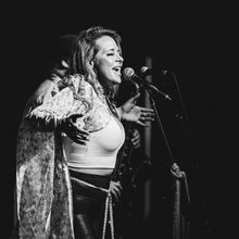 Load image into Gallery viewer, Black and white photo of a woman singing into a microphone on stage.
