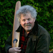 Load image into Gallery viewer, Man holding a wooden paddle with a bat logo against a green hedge background

